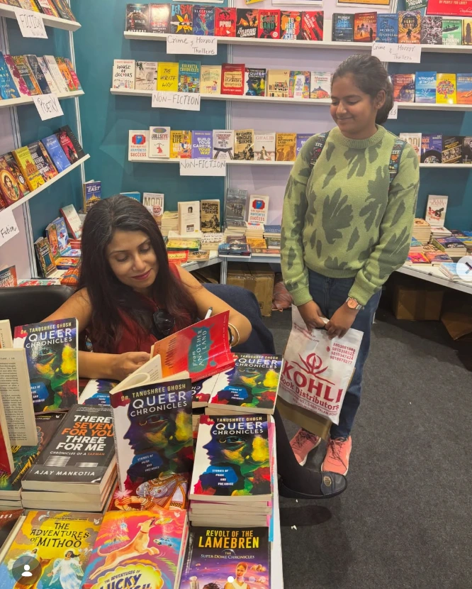 Tanushree Ghosh sharing a book with a reader at a bookshop, surrounded by copies of Queer Chronicles